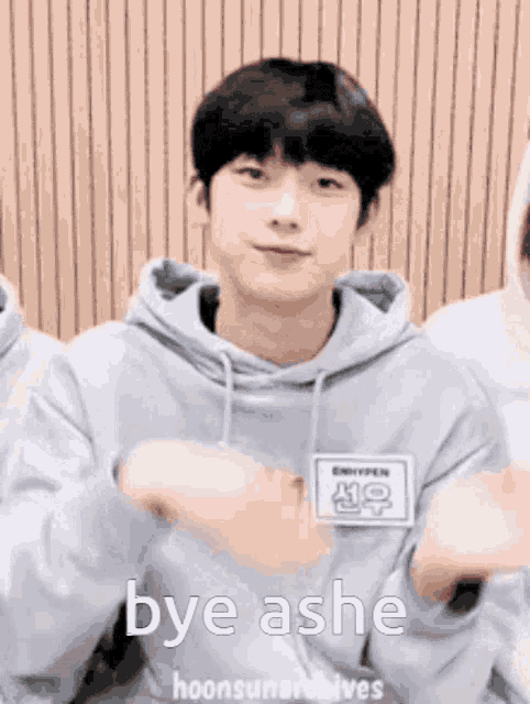 a young man in a gray hoodie is making a funny face and saying bye ashe .