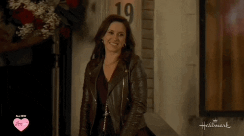 a woman wearing a leather jacket is standing in front of a hallmark sign
