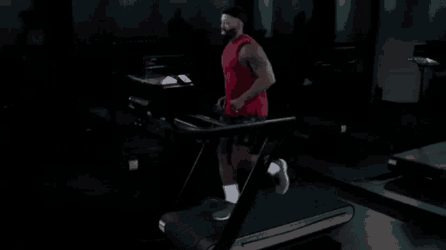 a man in a red tank top is running on a treadmill in a dark gym .