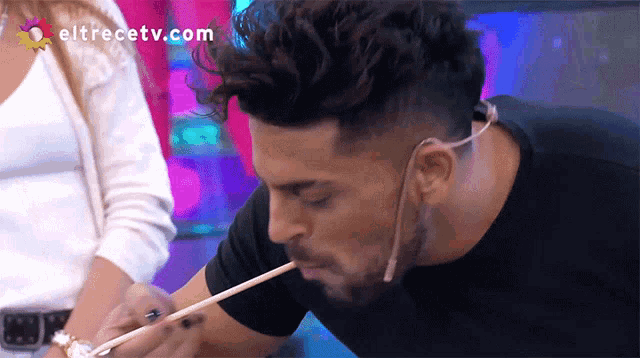 a man is eating something with a chopstick and the website eltrecetv.com is visible in the corner