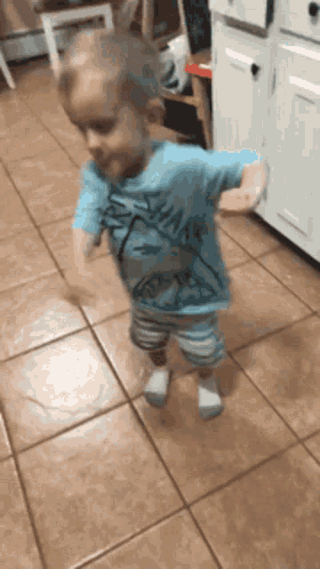 a little boy wearing a shark shirt is dancing on a tiled floor