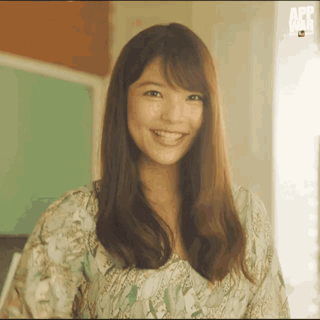 a woman in a floral dress is smiling in front of a green board that says app war