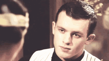 a man in a striped suit and black tie is looking at another man in a headband .