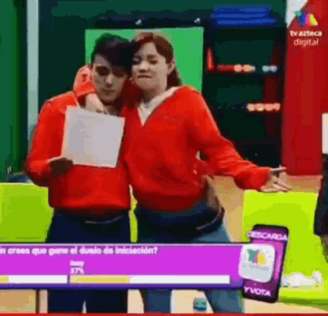 a man and a woman are standing next to each other in front of a tv screen that says descarga y vota