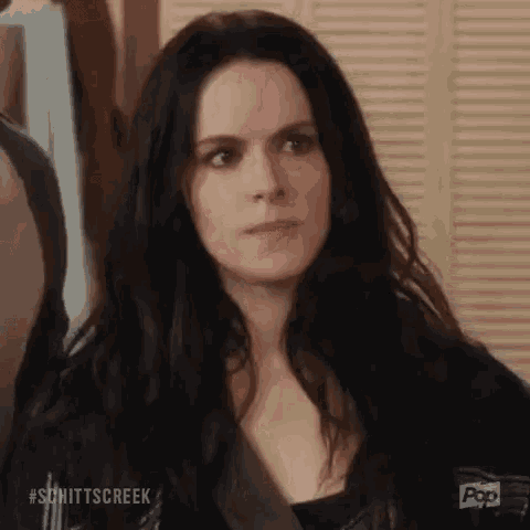 a woman with long black hair is standing in front of a wooden door and looking at the camera .