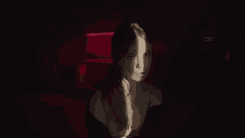 a woman in a black dress is standing in a dark room with a red light shining on her face .