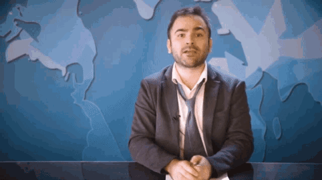 a man in a suit and tie is sitting in front of a blue map of the world