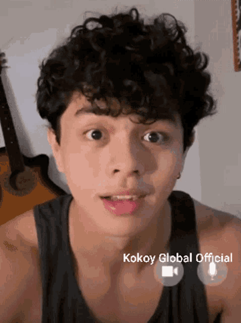 a young man with curly hair is wearing a black tank top with the words kokoy global official on the bottom