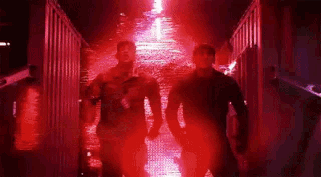 two men are walking through a tunnel with red lights coming out of it .