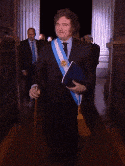 a man in a suit with a blue and white sash