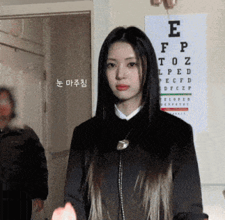 a woman stands in front of an eye chart with the letter e visible