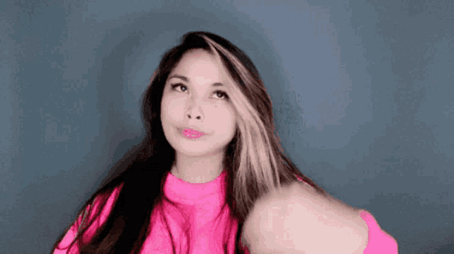 a woman is wearing a pink sweater and holding her hair