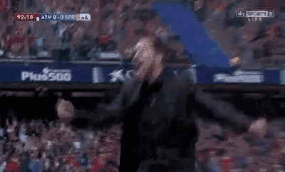 a man in a black suit is screaming in a dark room while watching a sports game on sky sports