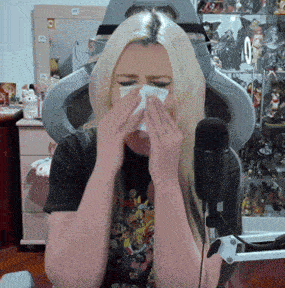 a woman is blowing her nose in front of a microphone while wearing a mask
