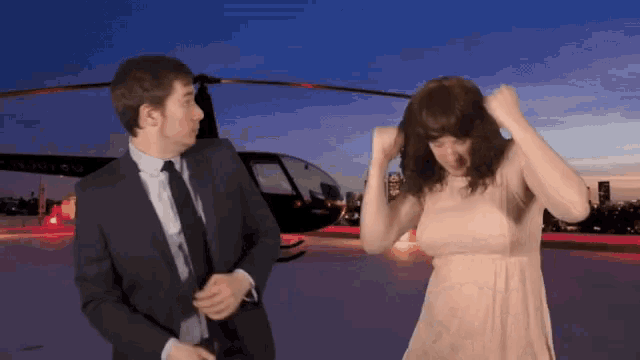 a man in a suit and tie is standing next to a woman in a dress in front of a helicopter