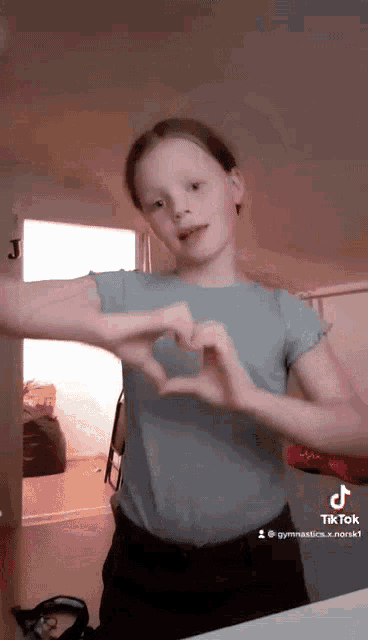 a young girl is making a heart shape with her hands