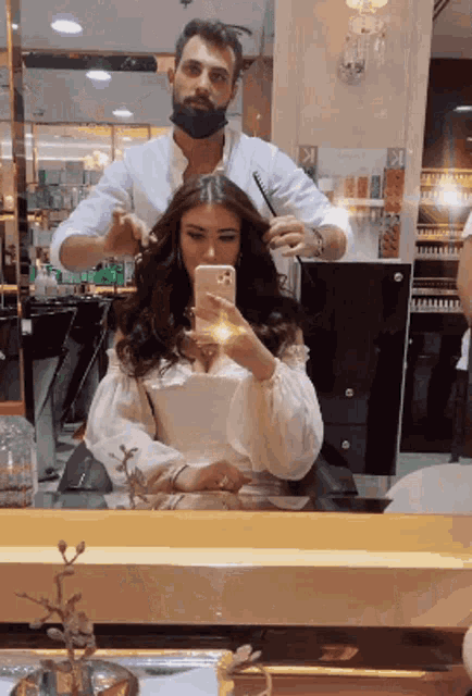 a woman taking a picture of herself in a mirror while getting her hair cut