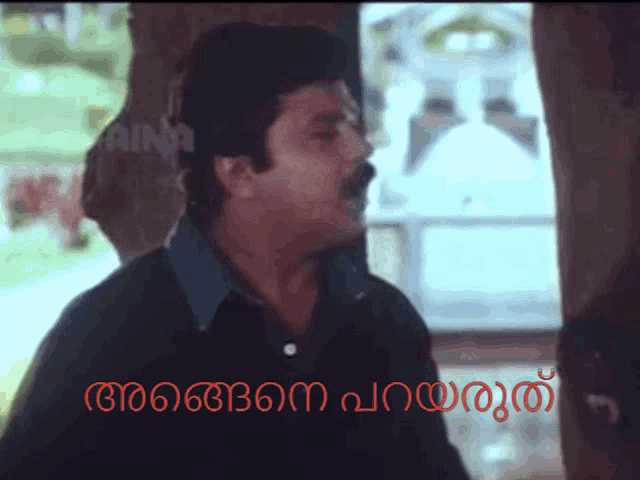 a man with a mustache is standing in front of a sign that says ' aina '