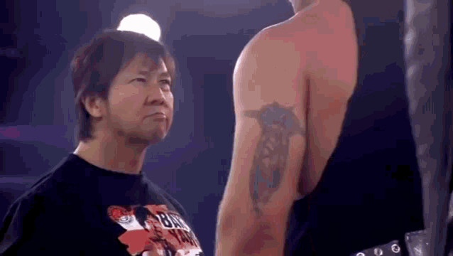 a man with a tattoo on his arm is standing next to another man in a boxing ring .