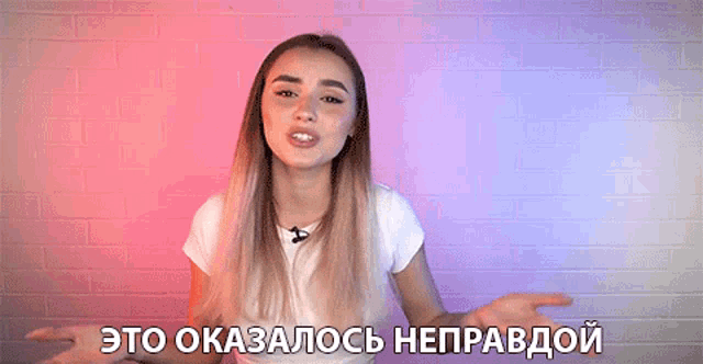 a woman in a white shirt stands in front of a brick wall with the words " это оказалось неправдой " written below her