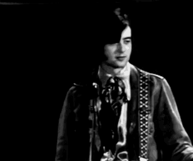 a man in a suit and tie is singing into a microphone while playing a guitar .