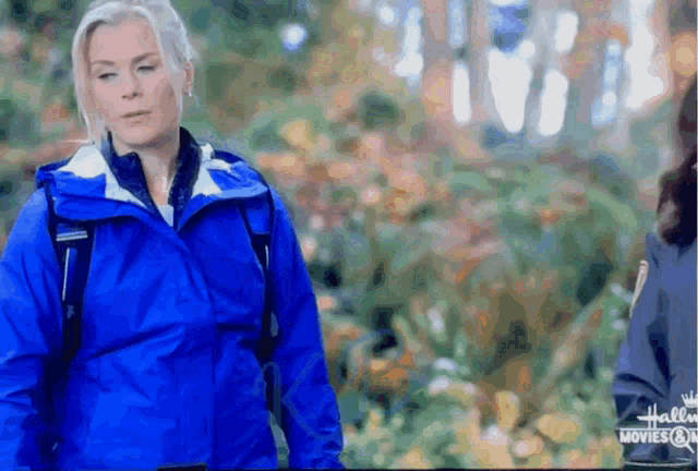 a woman in a blue jacket is walking in the woods