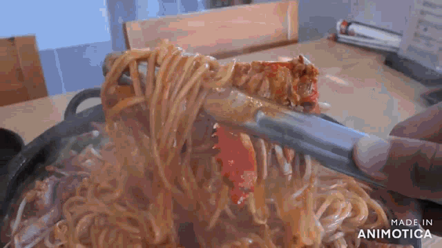 a person is holding a piece of meat over a bowl of noodles with tongs ..