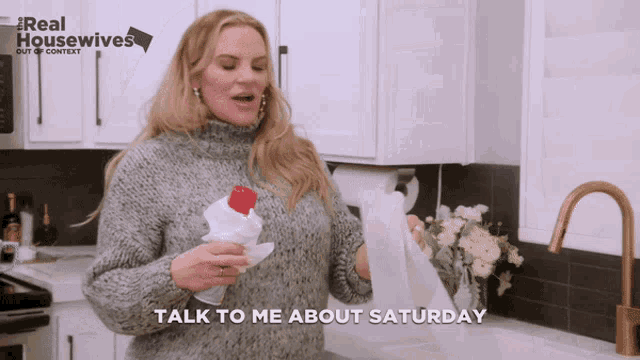 a woman in a kitchen holding a bottle and a roll of toilet paper with the words talk to me about saturday above her
