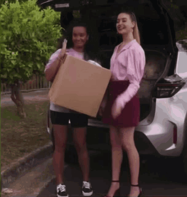 two women are standing next to each other in front of a car .