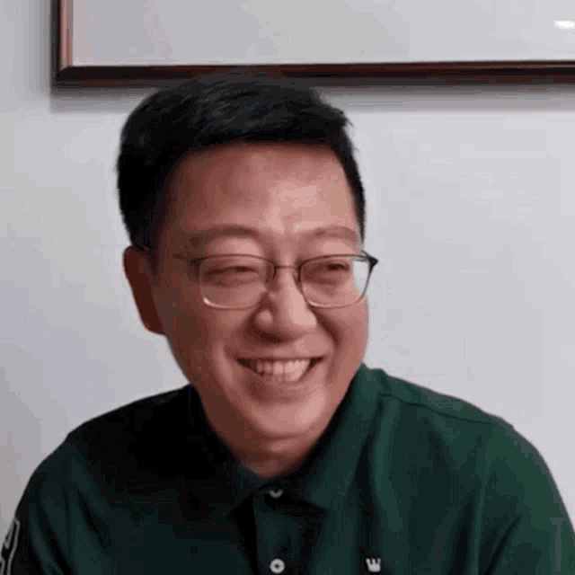 a close up of a man wearing glasses and a green shirt smiling .
