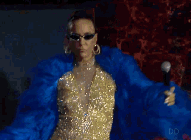 a woman wearing sunglasses and a blue coat is holding a microphone