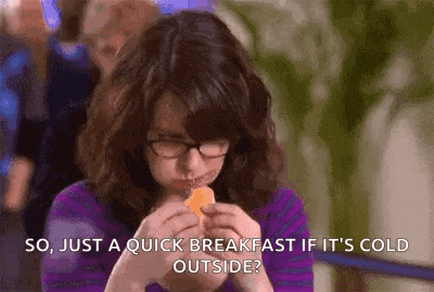 a woman wearing glasses is eating a piece of cheese while sitting at a table .
