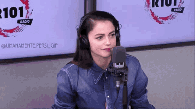 a woman wearing headphones stands in front of a microphone at riot radio