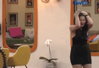 a woman in a black dress is standing in front of a mirror with gma on the wall behind her
