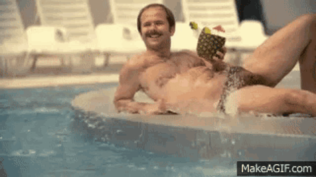 a shirtless man is laying in a pool holding a pineapple cocktail .