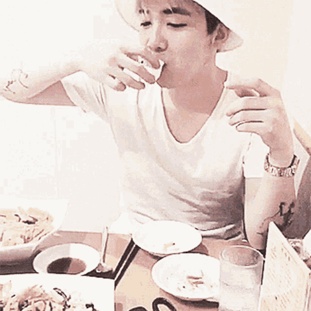 a man wearing a hat is drinking from a cup while sitting at a table with plates of food