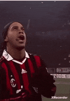 a soccer player in a red and black adidas jersey is standing on a field .