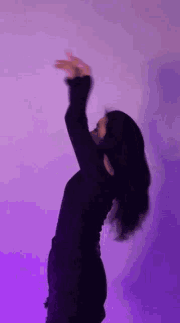 a woman in a black top is dancing in front of a purple background