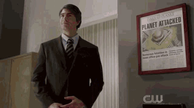 a man in a suit and tie stands in front of a framed newspaper that says planet attacked .