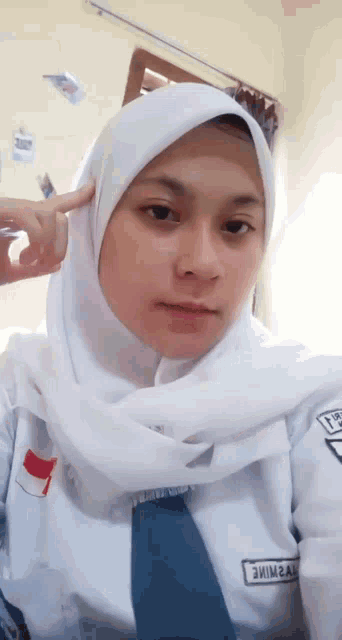 a girl wearing a white hijab is taking a selfie in a room .