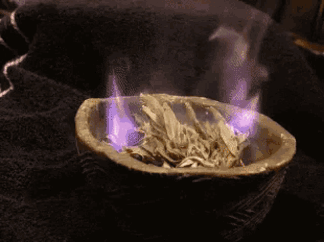 a bowl of white sage is burning with purple flames