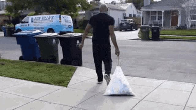 a man is carrying a large bag of trash down a sidewalk .
