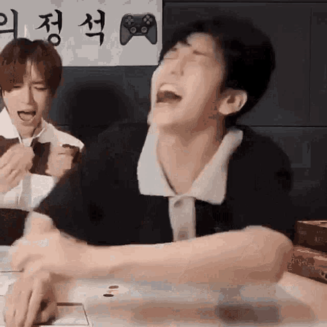 a man is sitting at a table with his mouth open and laughing while another man looks on .