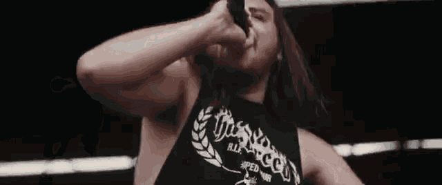 a man with long hair is singing into a microphone while wearing a tank top that says r.i.p.