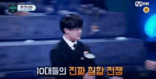 a man in a suit and tie is standing in front of a mnet sign .