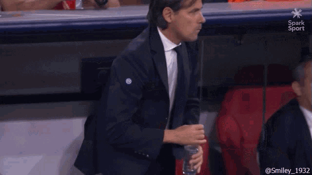 a man in a suit is sitting in a stadium holding a bottle