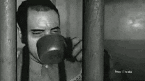 a man is drinking from a cup behind bars in a black and white photo .
