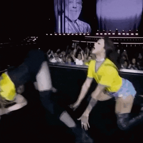 a couple of women are dancing on a stage in front of a crowd of people .