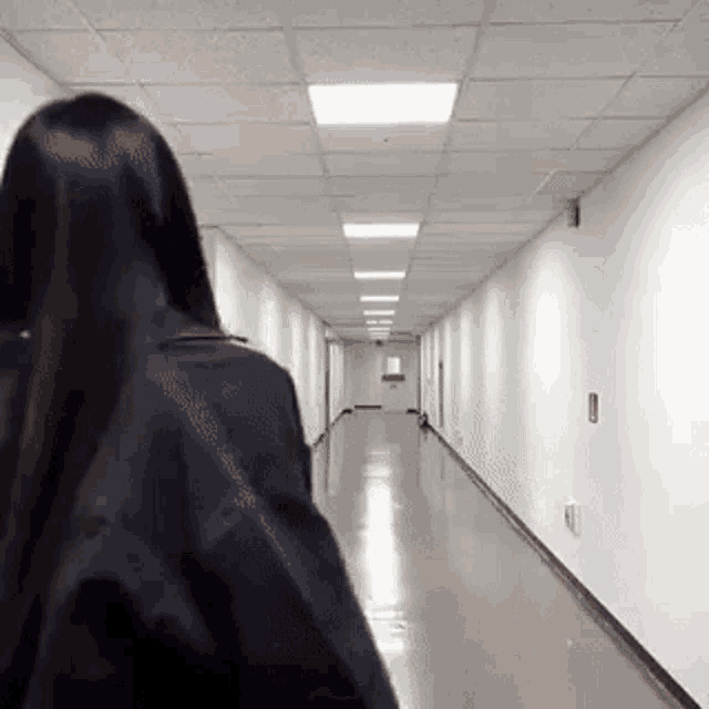 a woman walking down a long hallway with a backpack