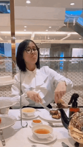 a woman wearing glasses sits at a table with plates of food and a teapot